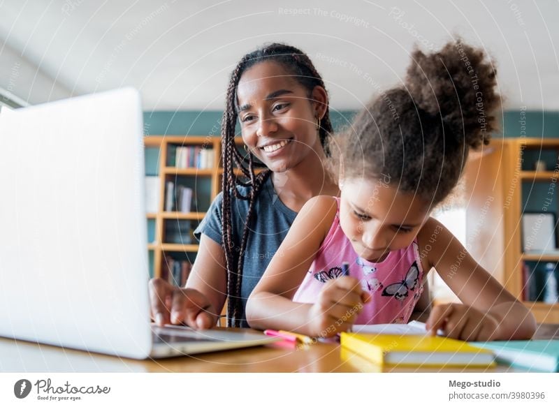 A mother helping her daughter with homeschool. laptop online homework student learning lifestyle quarantine family children people lock down indoor motherhood