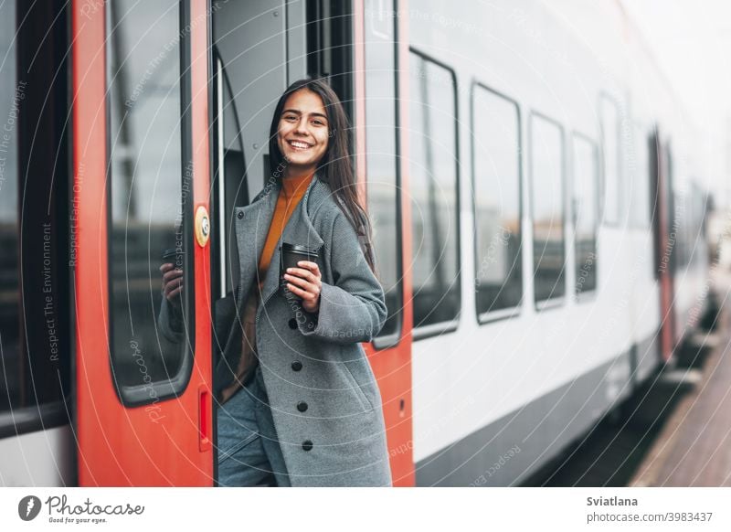 Happy girl enters the train at the station with coffee in her hands. transport young female beautiful railway passenger metro woman smiling public waiting