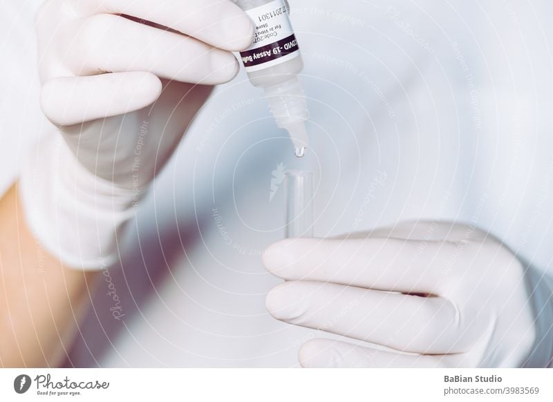 A nurse wearing latex gloves puts drops from the serological bottle into the tube and then rubs the swab to detect a covid-19 patient. assay buffer sample