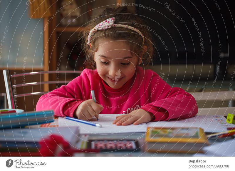 Smiling 6 year old girl does her homework child smiling write writing table case colors pens learning study schoolgirl desk childhood lesson student studying