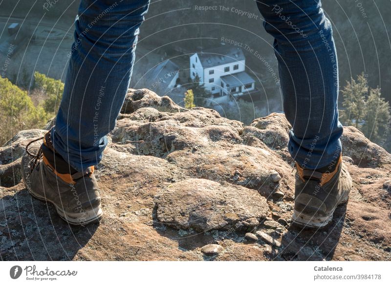 Looking down on a building at the foot of a rock in the shady valley Legs feet Pants Jeans sneakers Hiking boots Building Farm Architecture Stand Rock Stone