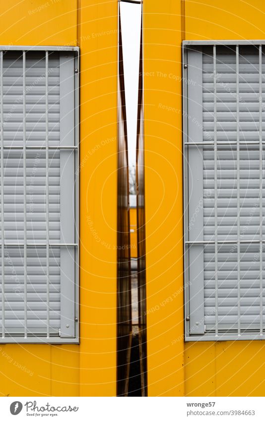 View through the free gap between 2 yellow construction containers with closed and barred windows Container Yellow containers Free space fissure Vista narrow