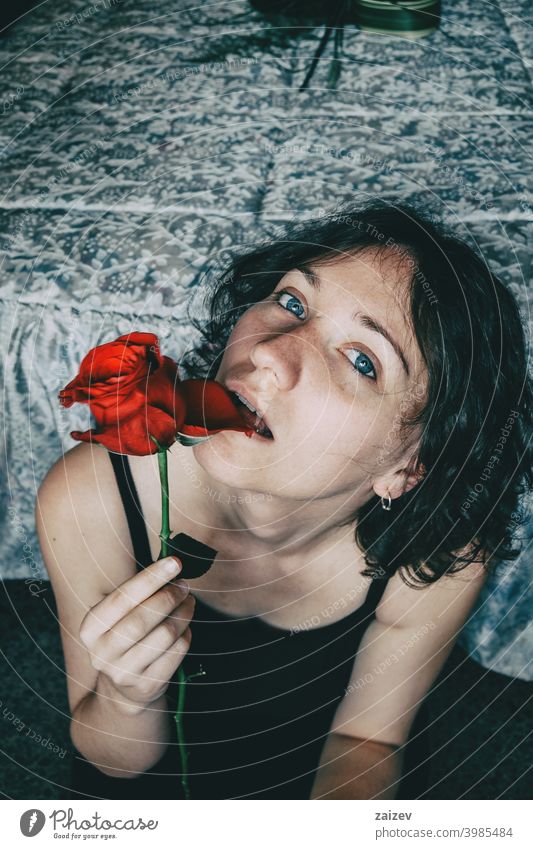 Portrait of blue-eyed beautiful girl biting a petal of a red rose sensually woman lady teen teenager youth young pretty eye contact looking at camera blue eyes