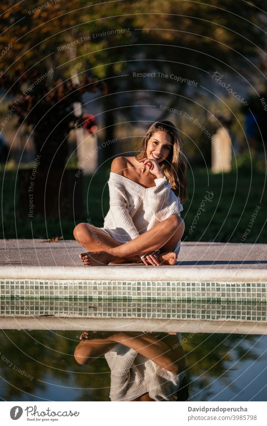 Crop woman resting near pool reflection water smile happy yard daytime calm legs crossed barefoot summer sit relax poolside lifestyle cheerful idyllic