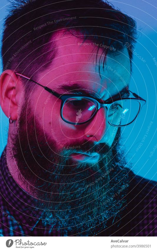 A young hipster male with blue light glasses looking away to camera with a serious face on blue and pink colors 20s contemplation entrepreneur genius technology