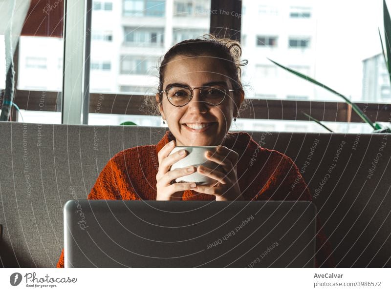 A young woman smiling in front of his laptop in the couch while he holds a cup of coffee Documents Horizontal job living relaxed Research Successful Teacher