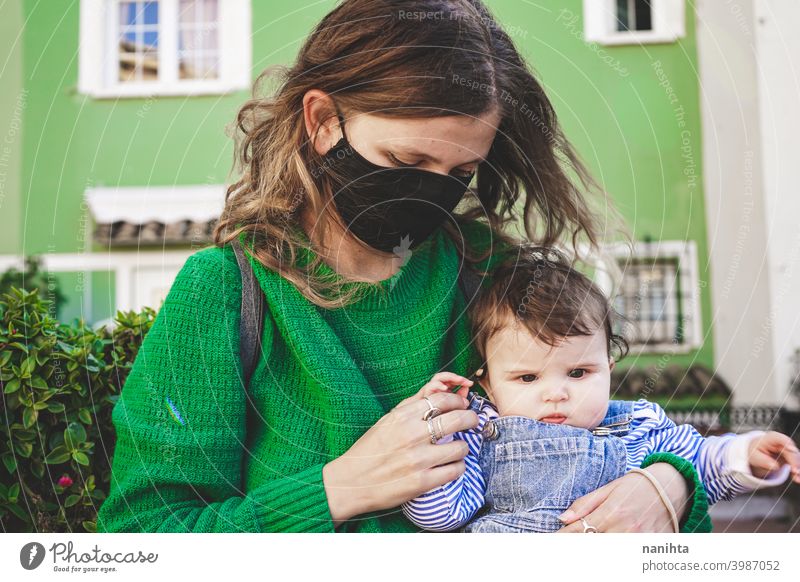 Image in green tones of a young single mom with her baby during covid pandemic coronavirus mother family motherhood mask face mask risk contagious influenza