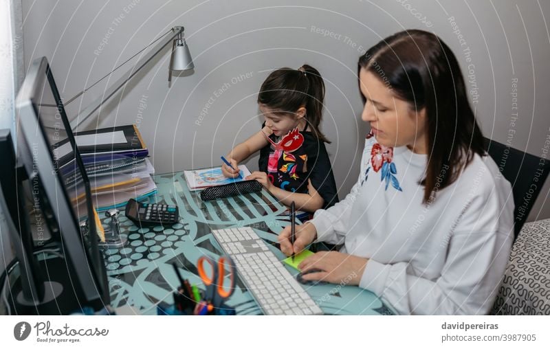 Woman teleworking with her daughter drawing family work reconciliation woman home working coronavirus quarantine writing a note computer epidemic mother