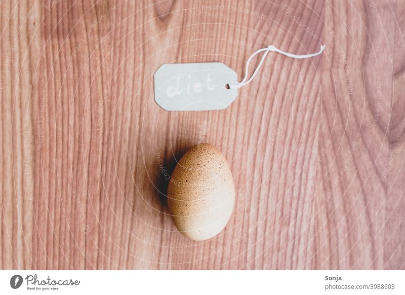 A brown egg and a label with the word diet on a wooden table Label Individual Egg Brown Protein high-protein protein source Fresh Organic Food Healthy Breakfast
