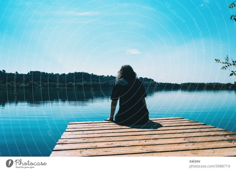 girl sitting on the edge of Banyoles lake with the landscape reflected in the water harmony meditation relaxing horizontal profile tranquility person