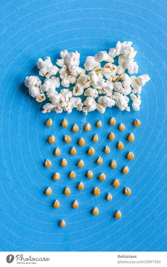 Large popcorn cloud with rain made out of corn kernels on blue background motion picture sky creative food yellow snack art white tasty hip diet weather lay