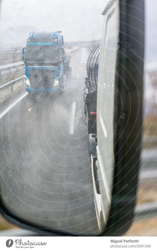 Rear view mirror of a truck on a rainy day with the blurred vision of another truck passing by. Truck Transport Overtake Side Rain Street Mirror Rear side