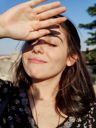Girl with the eyes closed covering the sun with her hand. health dermatology female treatment worried sunshine hot facial summer wrinkle skin bright sunblock
