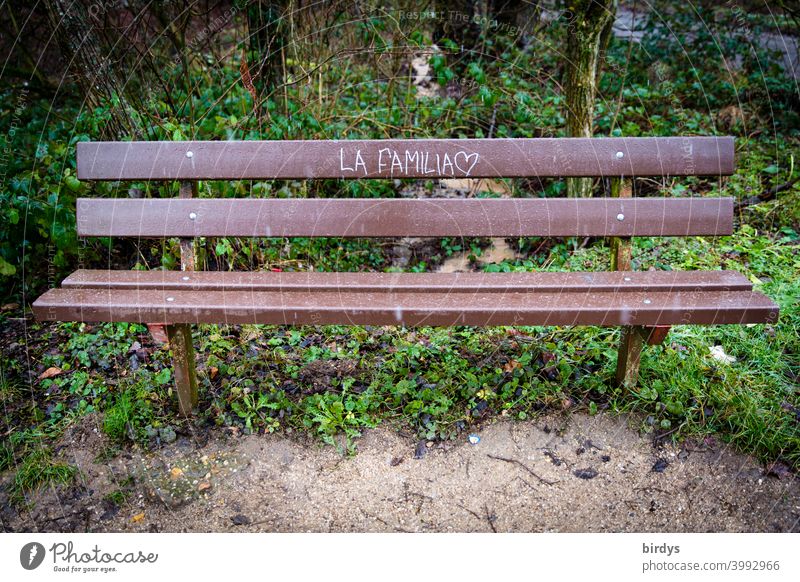 An empty park bench with the inscription " La Familia" with a heart . Family bench. Meeting place elective family Park bench Inscription Heart Choice Family
