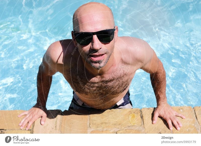 handsome guy half-naked cheerful man smiling laughing in blue water swimming pool wet tanned bald sunglasses summer young happy outside relaxation relaxing
