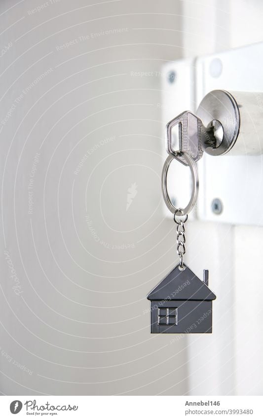 Silver house key in white door, with little keychain house, opening door to new house, home, investment, real estate concept, space for text security metal lock