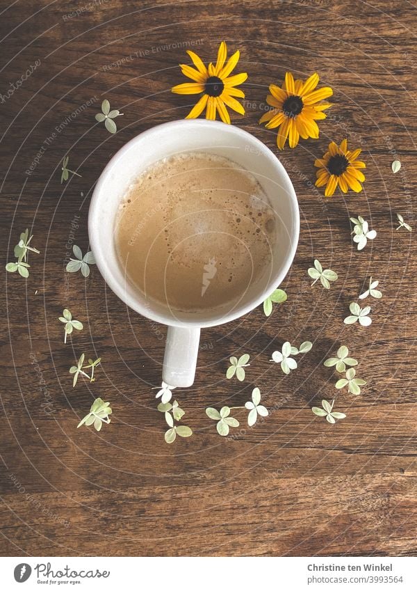 There is cappuccino for breakfast...  The wooden table is lovingly decorated with white and yellow scattered flowers Cappuccino Coffee Breakfast Café Cup