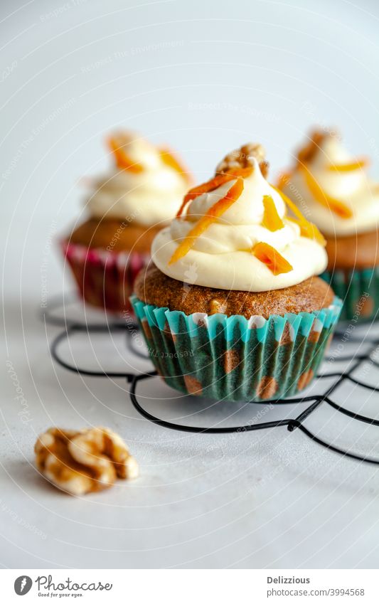 three carrot cake muffin with icing and carrot shaving on cooling rack white background bake bakery birthday blue bright brown celebration cinnamon copy space