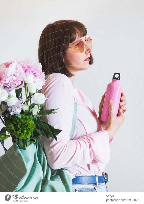 Young woman in pink with backpack and reusable bottle zero waste spring flowers summer sunglasses water thermos authentic face lifestyle womens day bouquet
