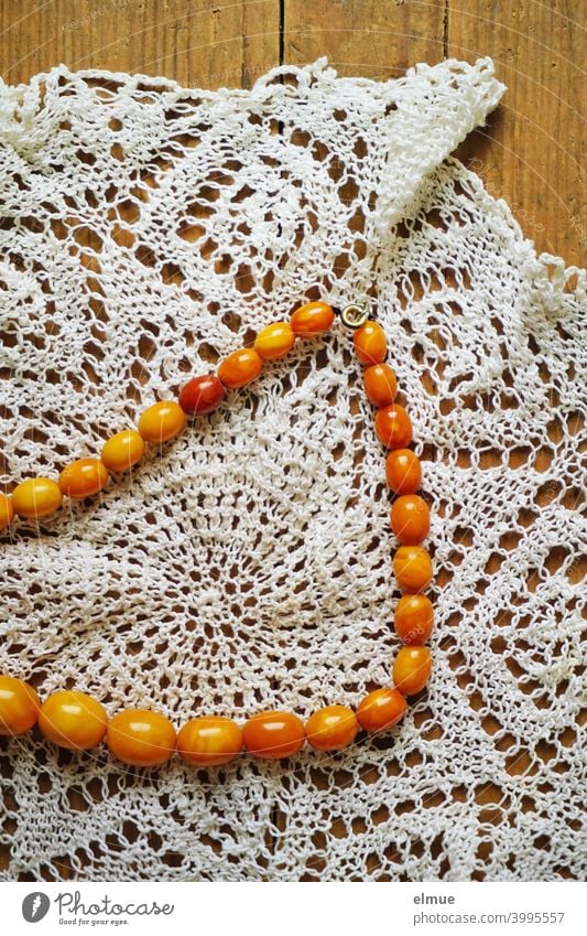 amber pearl necklace on a hand crocheted doily / jewelry / necklace Chain Pearl necklace Amber coloured Doily handcrafted Wooden table Handcrafts Jewellery