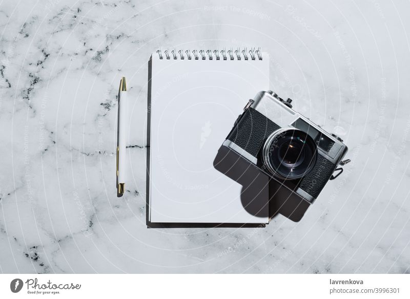 Flatlay of vintage film camera and notebook with pen on marble retro top view business table home diary freelancer items workplace mock up background blogger