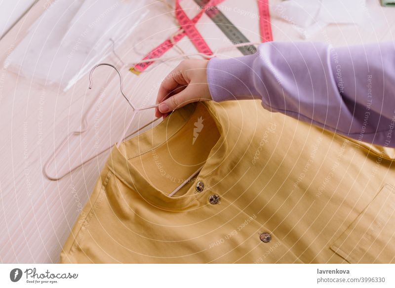 Top view of hands of female seamstress holding finished yellow shirt on a hanger workshop job entrepreneur woman girl tailor sewing person business professional