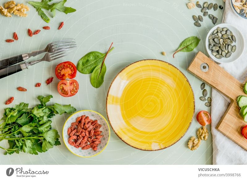 Blank yellow plate on green table with forks and healthy salad ingredients. Top view. Healthy lunch preparation blank top view group meal vegetarian organic