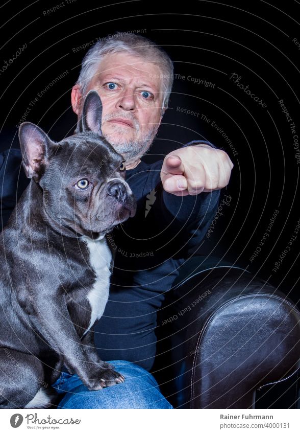 Best friends, dog and human. A man points his finger and pays attention, the French Bulldog looks unconcerned. The background is black. Dog lapdog boyfriend