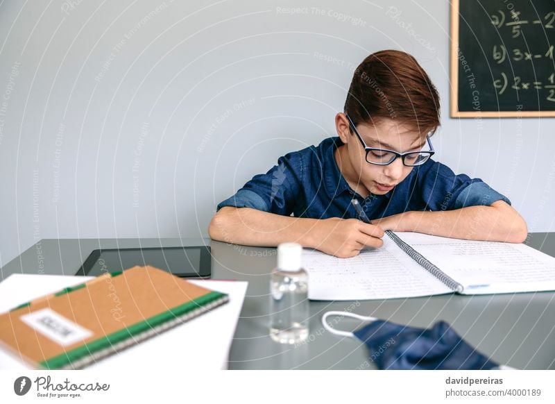 Boy writing in his notebook at school boy classroom mask on desk hand sanitizer coronavirus safety people student copy space education child epidemic no mask