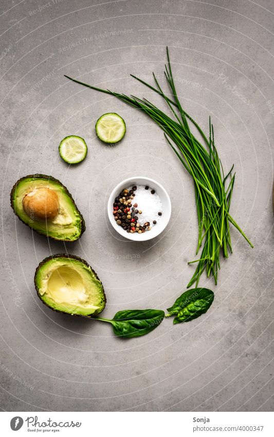 A bowl of salt and pepper and green vegetables and a halved avocado in a circle. Rustic background Vegetable Green Raw Circle Avocado flat lay