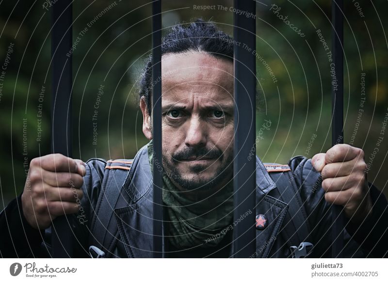 Portrait of angry man with angry look and clenched fists behind barred fence Force Masculine Brutal Facial hair Looking into the camera Iron gate Criminality
