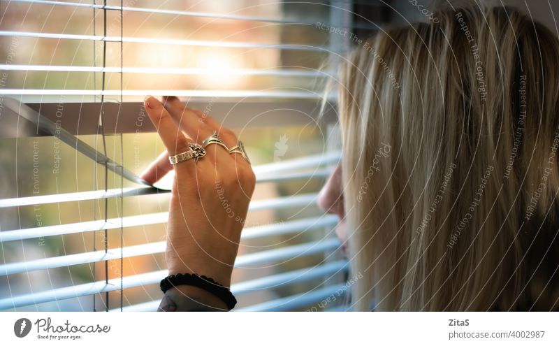 Blonde woman peeking through the window blinds blonde looking curious interior person hand life day shutters thinking spy privacy