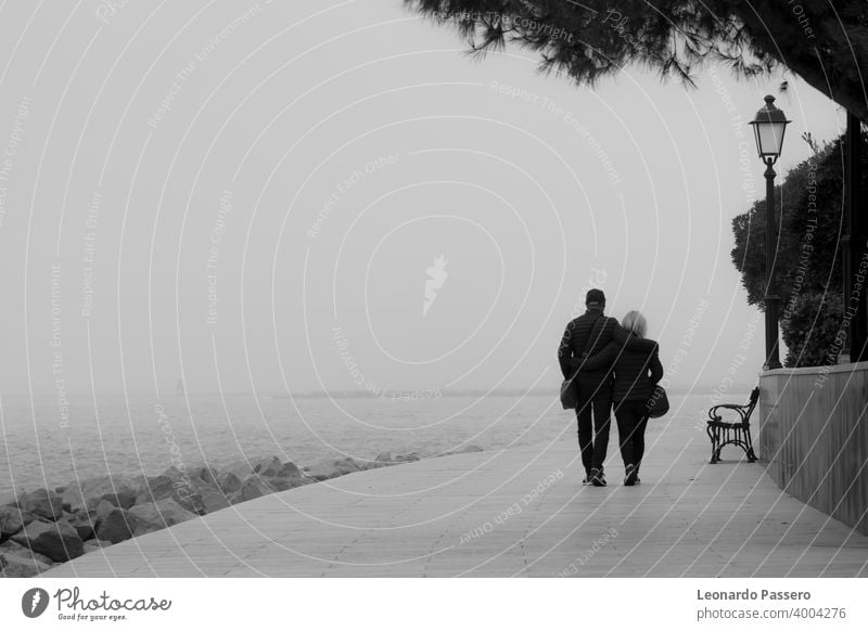 A couple walk along the waterfront on a foggy day - Grado, Italy Couple sea pier winter black and white Black and white photography black and white landscape