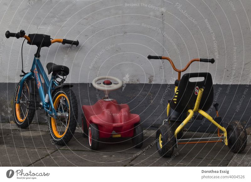 A child's bicycle, a slide car, a tricycle parked against a wall kita Children's vehicles Bicycle Bobbycar Tricycle Parked Toys out Exterior shot Colour photo