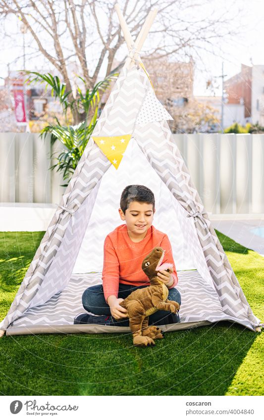 Little boy playing in a indian tent caucasian child childcare childhood clothes costume cute dinosaur educational feather fun funny game garden grass happiness