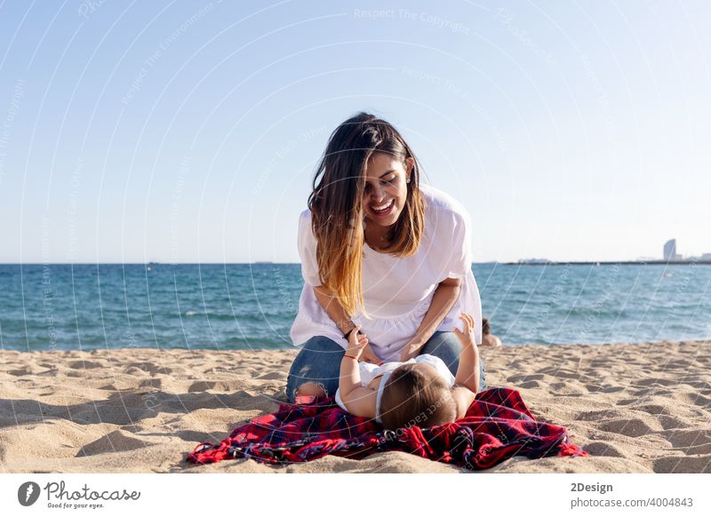 Smiling mom playing with newborn lying on beach towel baby love mother family happiness woman person smiling laughing sand sunlight together happy little summer