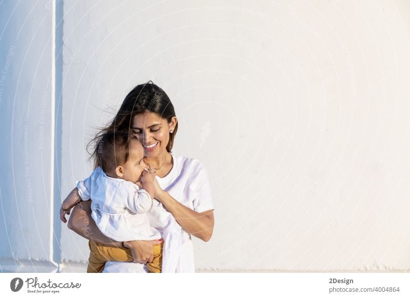 Young mother holding her little baby against white wall in sunny day child newborn love family woman care motherhood young childhood cute person happy girl