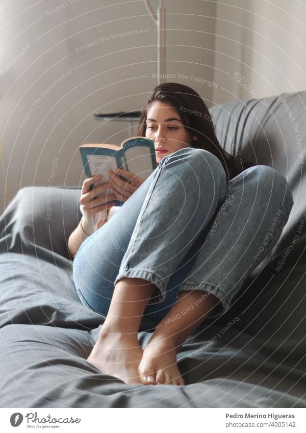 Woman reading on a sofa in a house home leisure sitting comfortable living room caucasian lifestyle brunette indoor domestic life casual attire happy woman
