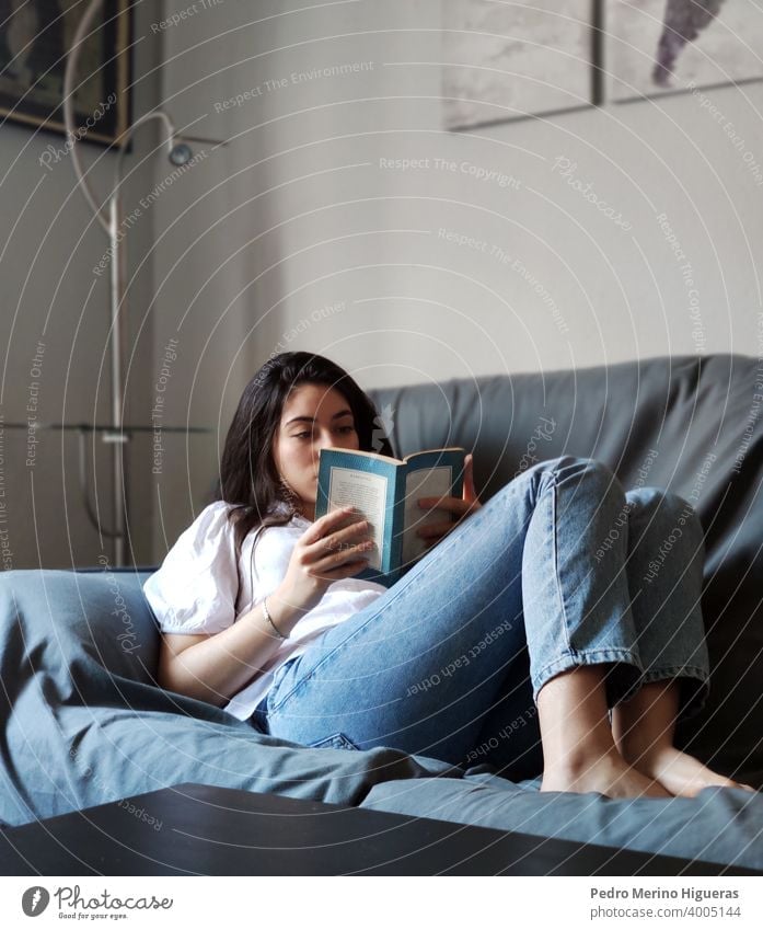 Woman reading on a sofa in a house home leisure sitting comfortable living room caucasian lifestyle brunette indoor domestic life casual attire happy woman