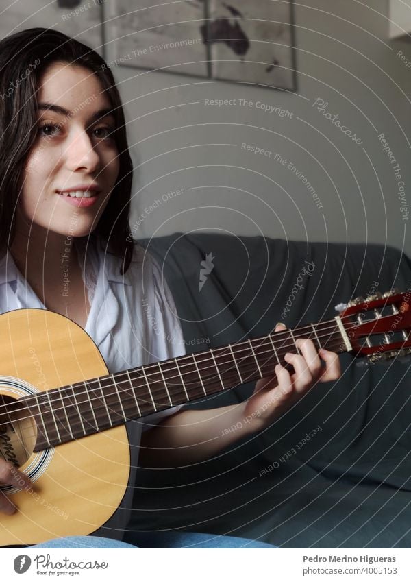 Woman playing the guitar on a gray sofa caucasian musical woman musician girl instrument background casual attire string studio young learning acoustic teenage