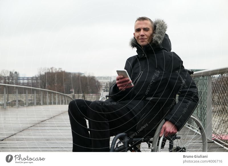 Concept of disabled person. Man in a wheelchair outside in the street. People using technology with smartphone. man equipment paraplegic connected assistance