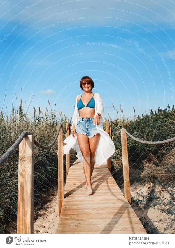 Young woman in cover up and jeans shorts walking between dunes. kimono white smile alone blue turquoise beach highwaist Travel vacations concept destination