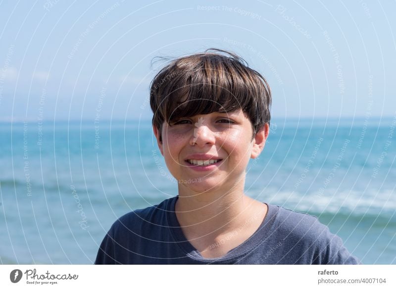 Portrait of a smiling male teen against blue sea caucasian portrait adolescence lifestyle beach young youth 1 person cute teenage hair summer boy cheerful