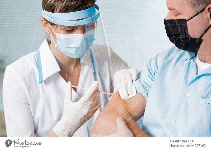 Female doctor with surgical mask and in gloves giving vaccine injection to man in hospital. Vaccination during COVID-19 pandemic arm care clinic coronavirus