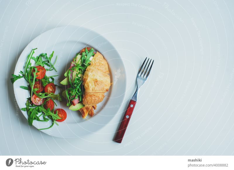 healthy tasty breakfast - croissant with avocado, arugula, ham and cheese served with cherry tomato salad on white plate sandwich food meal snack lunch