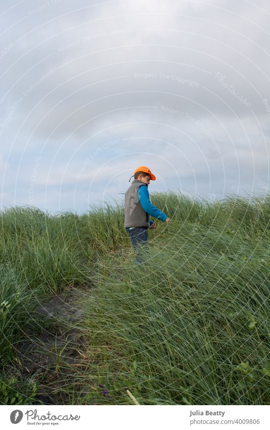 Young boy climbing a sand dune with grasses at the beach on cold day sandhill beach grass adventure kid cloudy oregon coast pacific pacific northwest sky nature