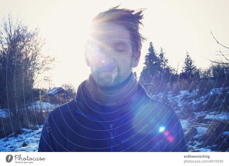 Man refueling in the sun (in winter landscape in backlight) Sun rays Face hair Cold chill warming Closed eyes Glare Blue relaxed To enjoy Dream Landscape Winter