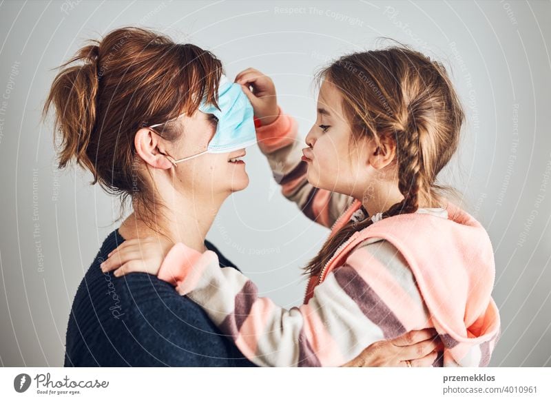 Little girl moving her mom's face mask on eyes and giving a kiss her mother. Funny moments during covid-19 pandemic affection affectionate bond care caucasian