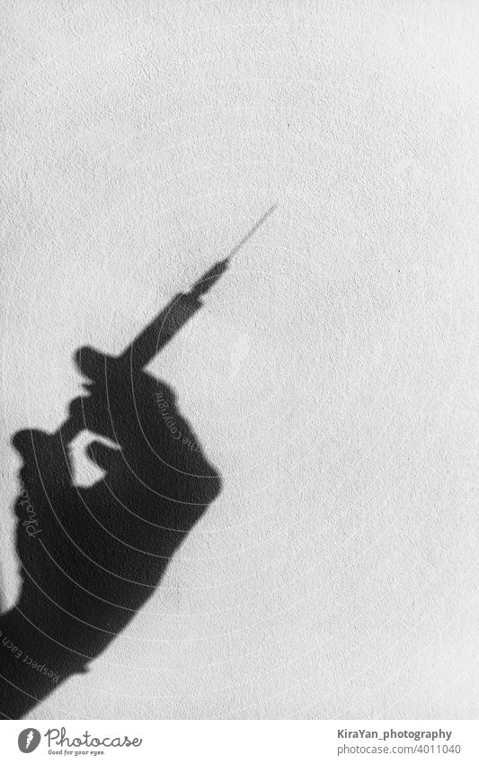 Shadow of a hand with a syringe on a white wall covid-19 coronavirus health vaccination concept medical black and white shadow copy space