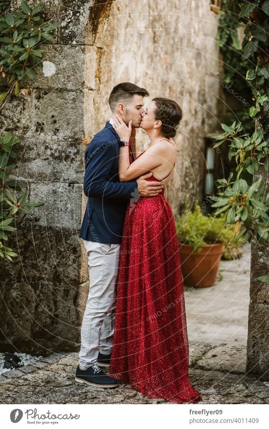 Elegant young couple on a luxurious building with vegetation elegant prom kiss 20s dress suit red first time event caucasian luxury castle ancient tuxedo